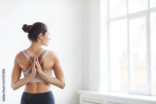 Rear view of young healthy woman hiding her hands behind back and meditating during yoga in the class