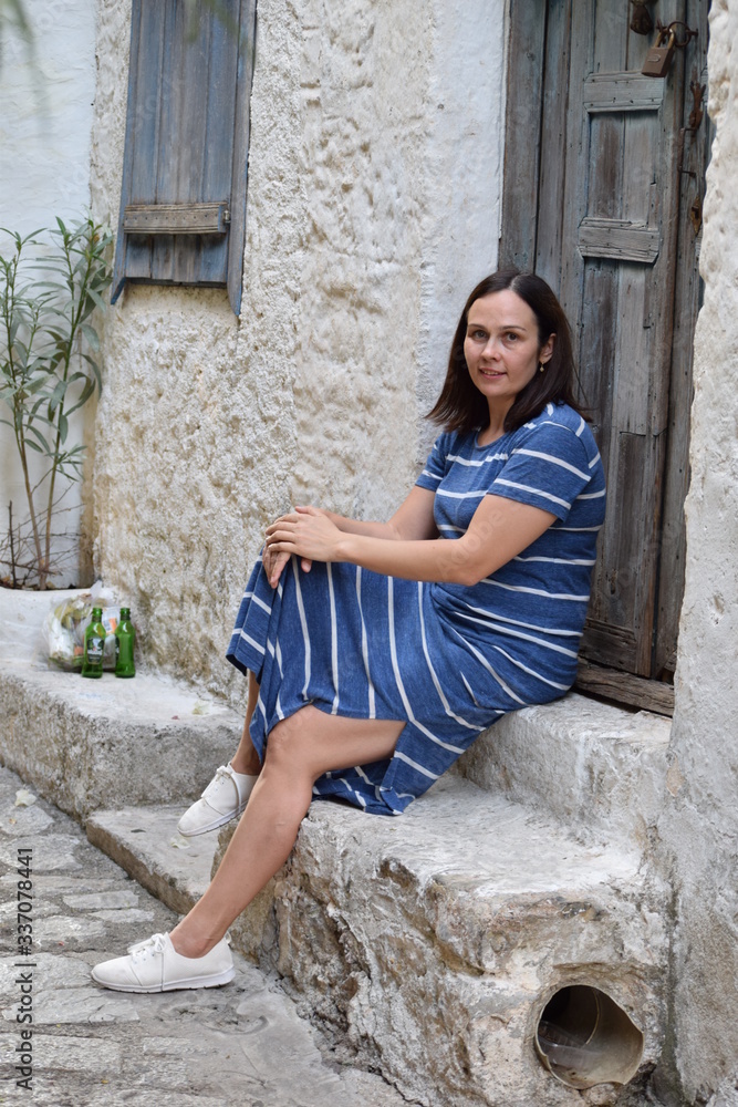 A brunette woman in a striped dress near the old door of an old house A brunette woman in a striped dress near the old door of an old house