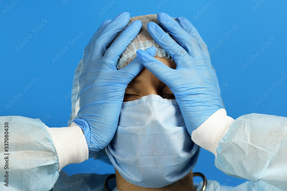 Fototapeta premium Attractive female doctor in a dressing gown , medical mask is upset, in a panic holding her hands to head