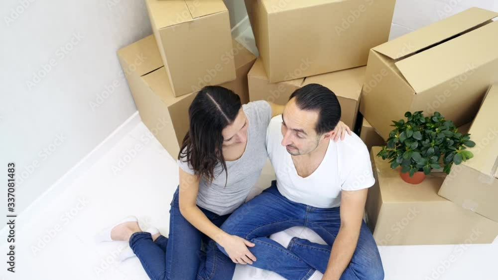 Top-view of young man and woman relaxing together in new house, sitting on the floor, leaning to stack of carton boxes. Top-view of young man and woman relaxing together in new house, sitting on the floor, leaning to stack of carton boxes.
