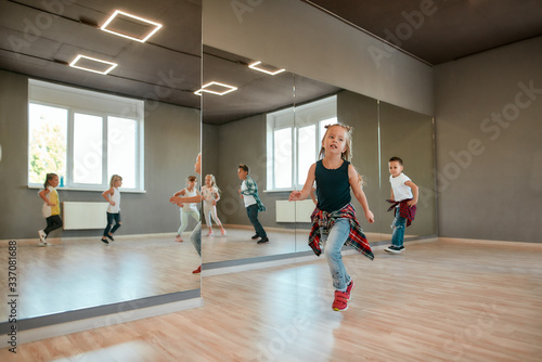 Portrait of little cute girl in casual clothes warming up before dance class in studio. Little and happy boys and girls running in the choreography class