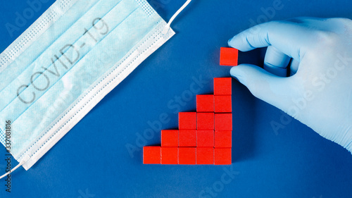 Hand in glove adding red cubes to growing column graph representing a rising number of infected or death toll of Corona Virus pandemic.