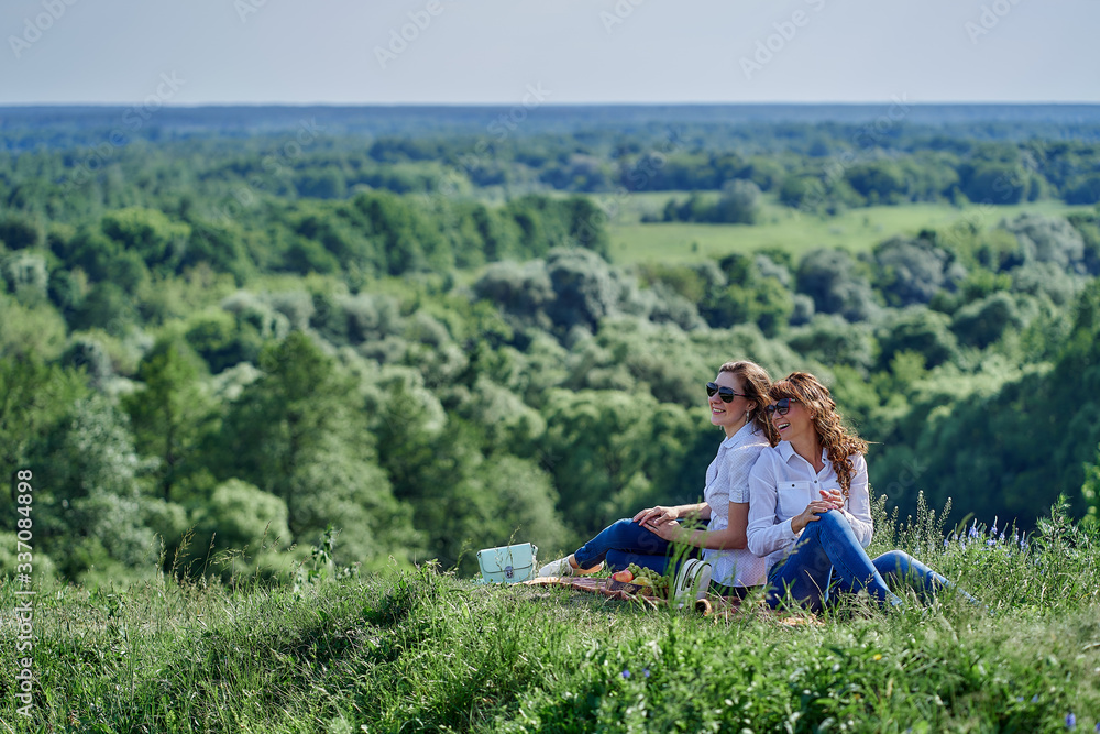 Two girls sit with their backs to each other in nature on picnic. Two girls sit with their backs to each other in nature on picnic.