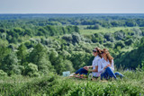 Two girls sit with their backs to each other in nature on picnic.
