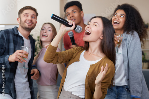 Singing Girl. Young beautiful asian woman holding microphone and singing while having fun with friends at home. Playing karaoke at home. Happy multicultural people spending time together
