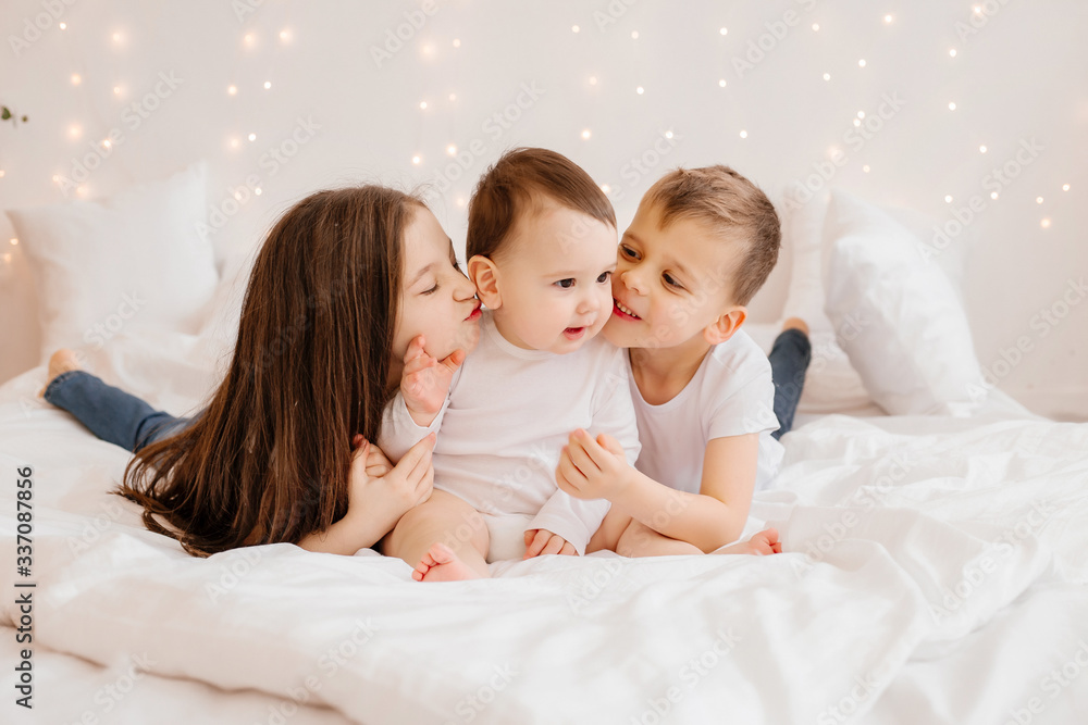 Three young children lie in bed and cuddle, view from above. siblings, large family Three young children lie in bed and cuddle, view from above. siblings, large family