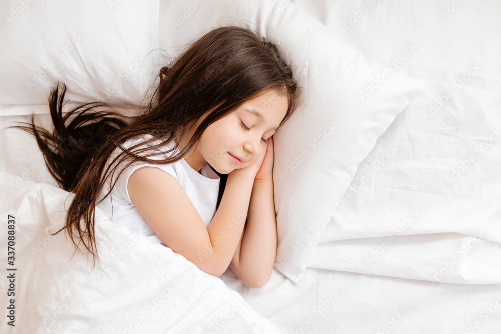 Little brunette girl sleeps sweetly in bed with white linen. space for text. healthy baby's sleep Little brunette girl sleeps sweetly in bed with white linen. space for text. healthy baby's sleep