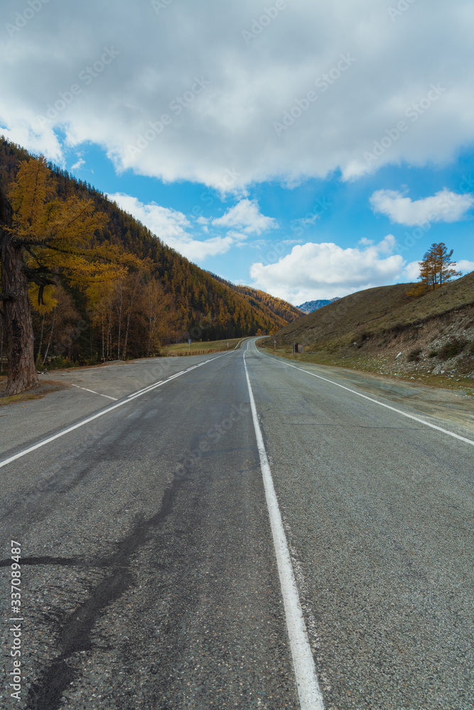 Road in the autumn mountains. Altai, Siberia, Russia. Yellow autumn forest and mountains with clouds.