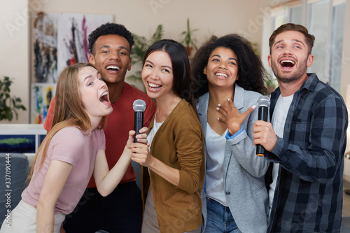 Best friends having fun. Group of young happy multicultural friends singing with microphone together, playing karaoke at home, spending nice time together. Karaoke party