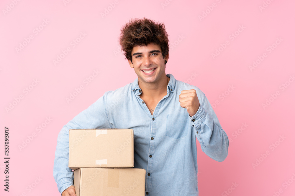 Young caucasian man over isolated pink background holding a box to move it to another site Young caucasian man over isolated pink background holding a box to move it to another site