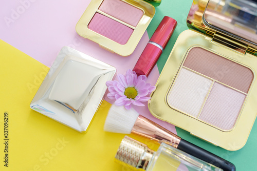 premium makeup brushes, red lipstick, bottle of perfume and blush pads on a bright colorful background, creative cosmetics flat lay