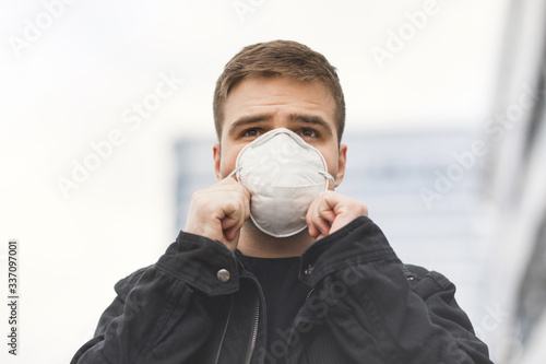 portrait of a young man in a surgical dressing on a modern building background, coronavirus, disease, infection, quarantine, medical mask © Aliaksandr