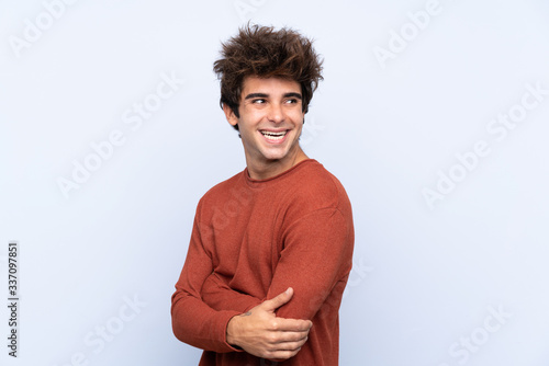 Young caucasian man over isolated blue background with arms crossed and happy