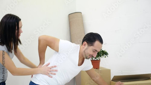 Tired guy is bringing heavy boxes in room suffering from backache touching back with unhappy face during relocation. photo