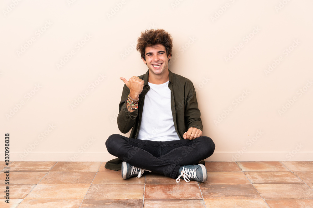 Young caucasian man sitting on the floor pointing to the side to present a product Young caucasian man sitting on the floor pointing to the side to present a product
