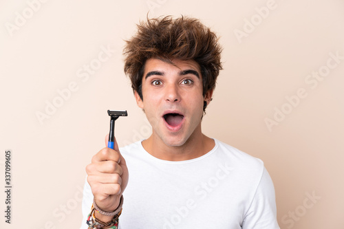 Young handsome man shaving his beard with surprise and shocked facial expression