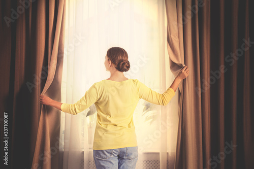 Woman opening window curtains at home in morning