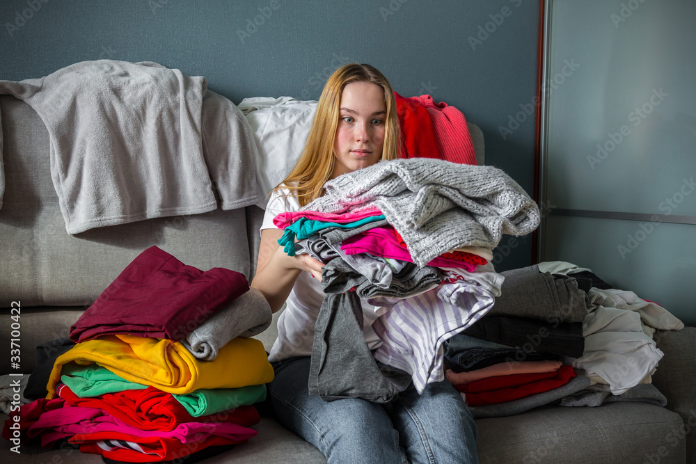 Obraz premium Fast fashion, the girl puts things in order in the closet. A bunch of colorful clothes. The concept of processing, second hand, eco, minimalism, consumption of goods.