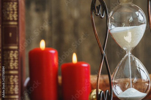 Hourglass and red burning candles close up on wooden desk