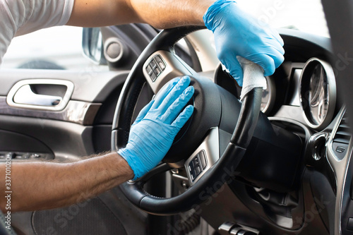 A bearded brown haired man wearing a baseball cap uses alcohol wipes to sterilize the front driver seat, steering wheel, and surrounding areas from any lingering virus strains or germs that are inside © Joshua
