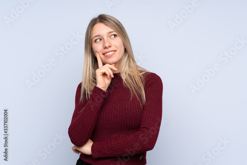 Young blonde woman over isolated blue background thinking an idea while looking up