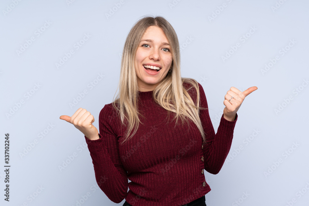 Young blonde woman over isolated blue background with thumbs up gesture and smiling Young blonde woman over isolated blue background with thumbs up gesture and smiling