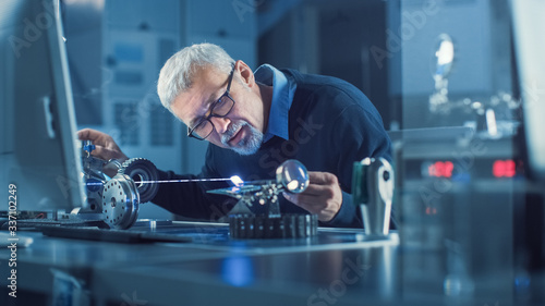 Portrait of Focused Middle Aged Engineer in Glasses Working with High Precision Laser Equipment, Using Lenses and Testing Optics for Accuracy Required Electronics photo