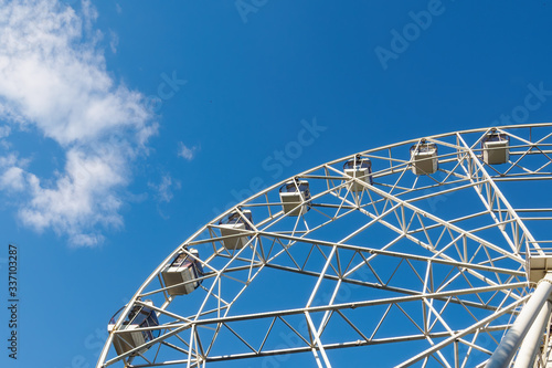 A part of white ferris wheel, cabins on background of blue sky and cloud in sunny summer day, bottom view.