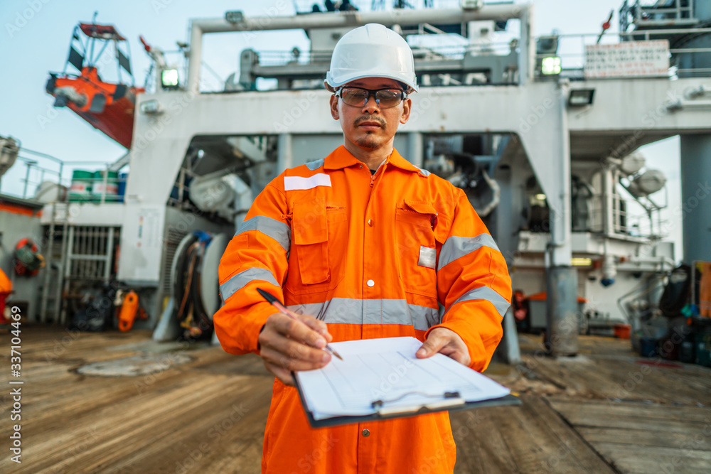 Filipino deck Officer on deck of offshore vessel or ship , wearing PPE personal protective equipment. He fills checklist. Paperwork at sea Filipino deck Officer on deck of offshore vessel or ship , wearing PPE personal protective equipment. He fills checklist. Paperwork at sea