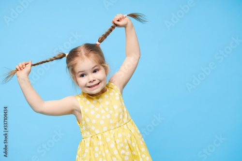 Portrait of surprised smiling cute little toddler girl. child standing isolated over blue background. Looking at camera and laughs