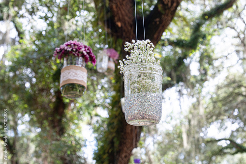 Various flowers in mason jars hanging from trees over wedding ceremony