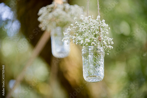 Babies breath in two clear mason jars with hanging from tree over wedding ceremony isle