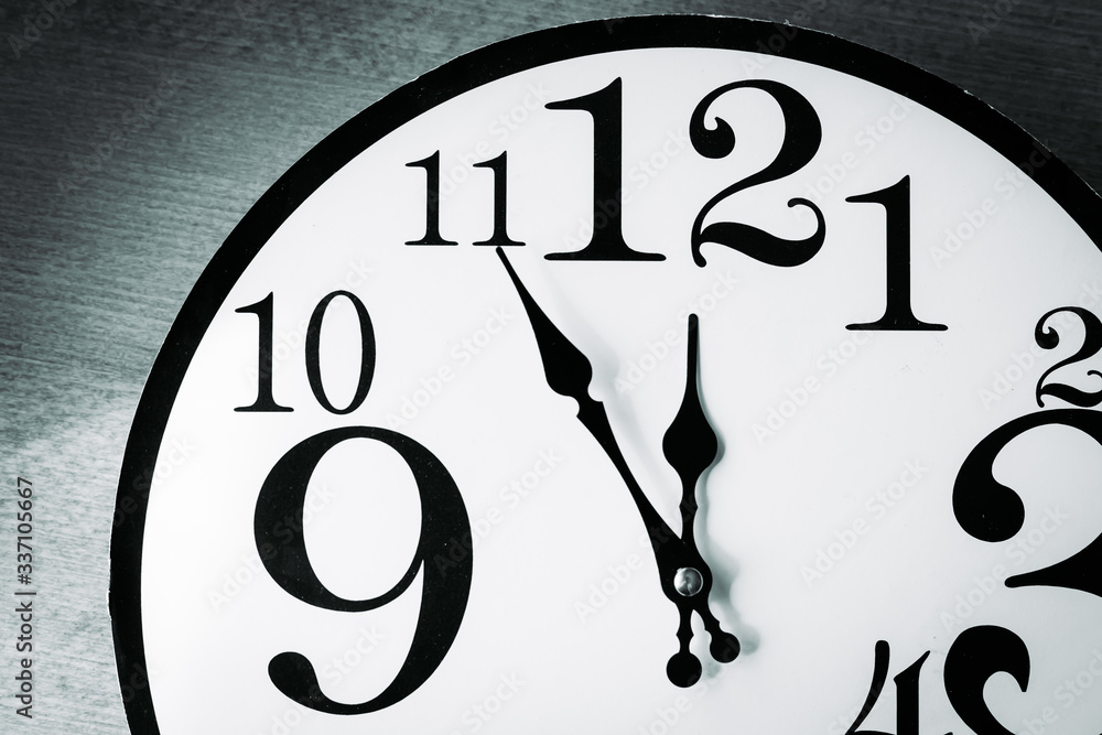 Black and white wall clock showing five minutes until 12 oclock Stock