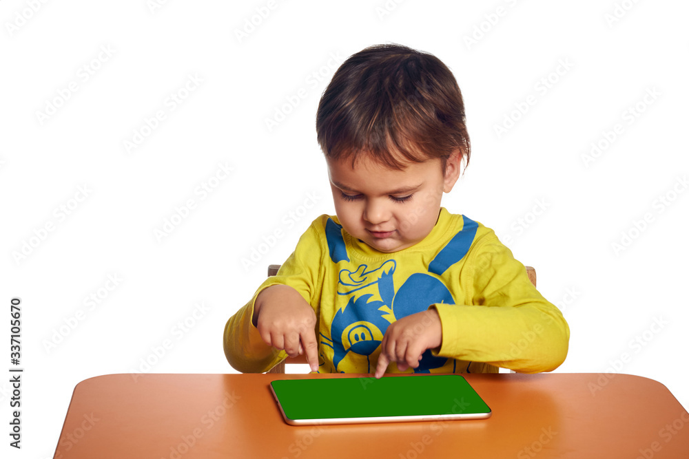 Young child girl is using tablet while sitting at table, isolated over white background Young child girl is using tablet while sitting at table, isolated over white background