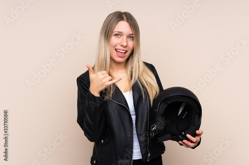 Young blonde woman with a motorcycle helmet over isolated background making phone gesture © luismolinero