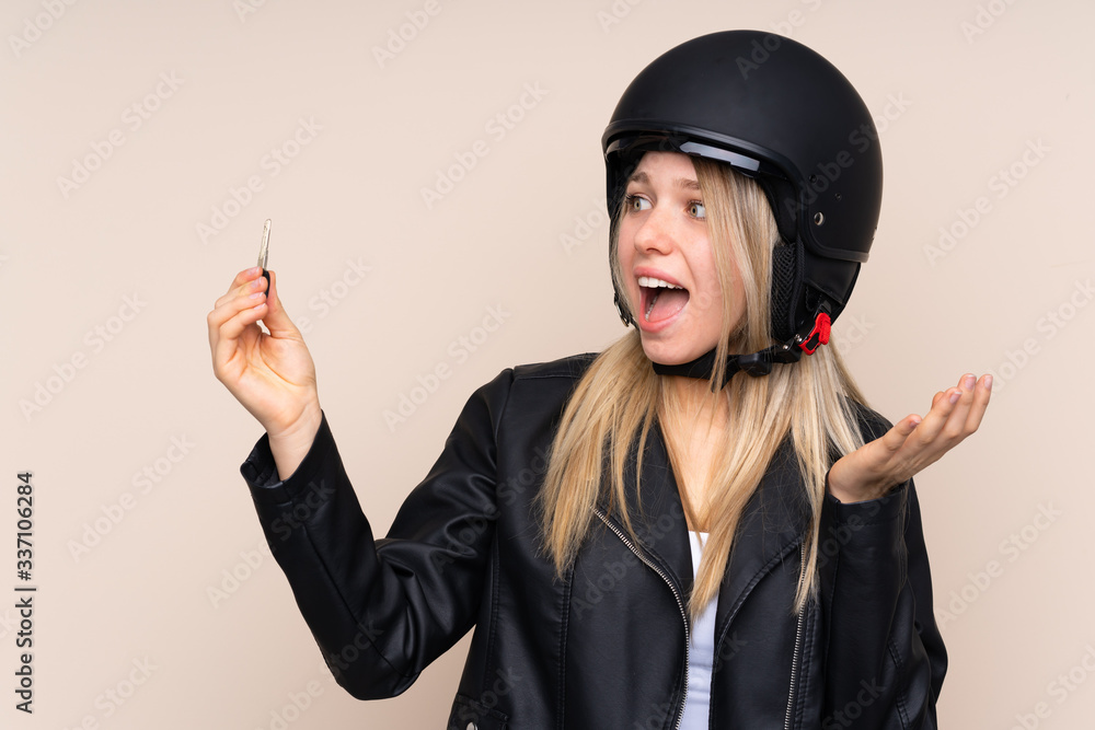 Young blonde woman with a motorcycle helmet and a key doing surprise gesture over isolated background Young blonde woman with a motorcycle helmet and a key doing surprise gesture over isolated background