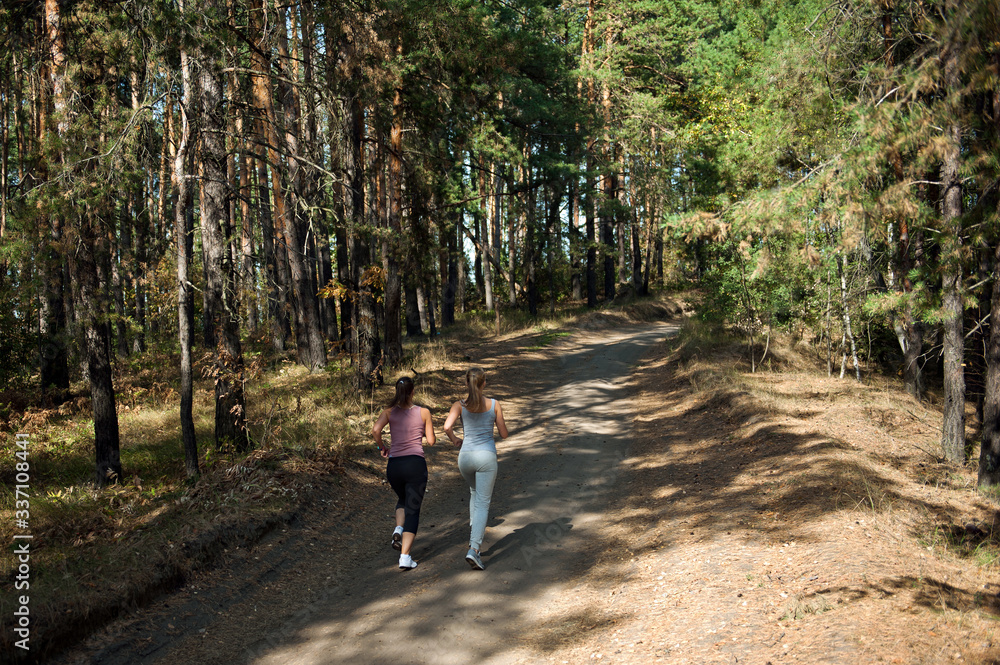 Two girls of the athlete perform a run in the morning in the sunny forest Two girls of the athlete perform a run in the morning in the sunny forest