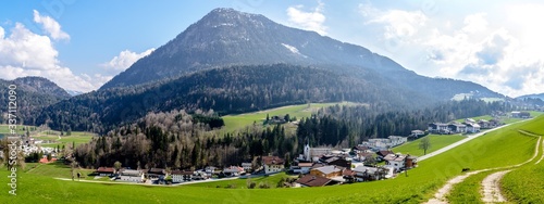 Alps mountains by lake Thiersee nearby Kufstein, mountain Barenhohle, Mittagskopf, blue sky, green field, church, houses. Tyrol, Austria. Panorama view  photo