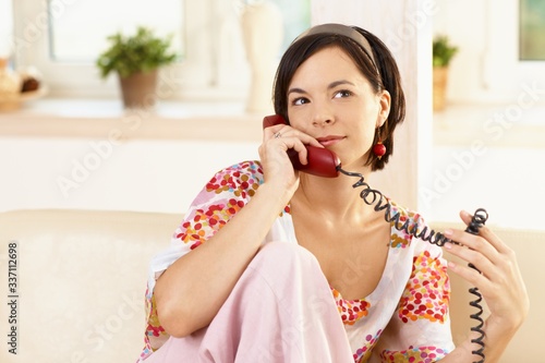 Portrait of happy young woman sitting on sofa at home, talking on landline phone.