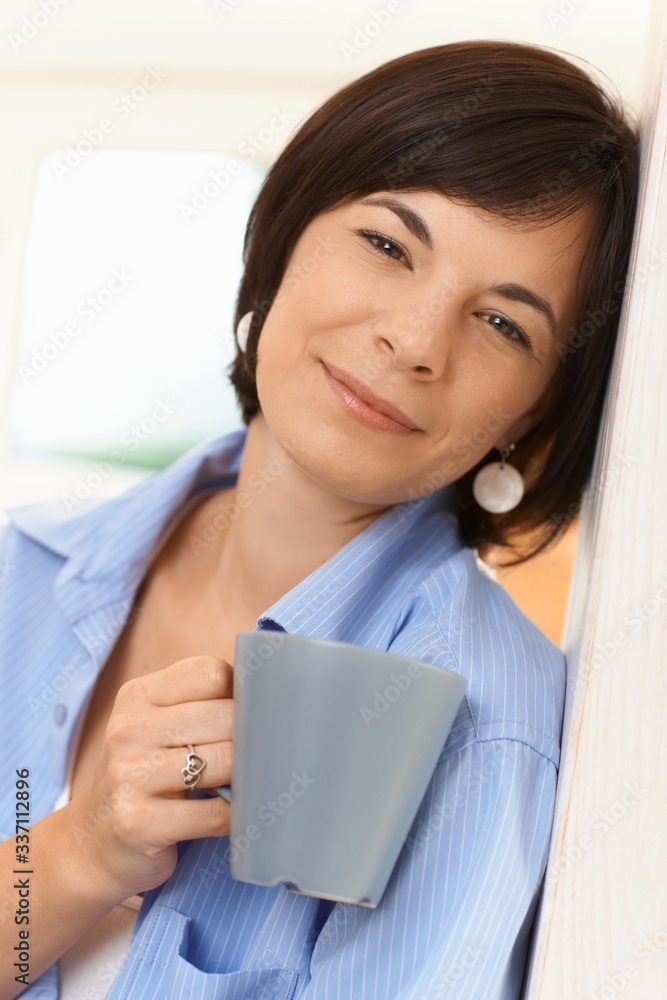 Portrait of casual young woman, looking at camera, holding tea cup, smiling Portrait of casual young woman, looking at camera, holding tea cup, smiling