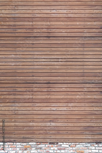 A solid wall of aged brown wooden planks with hammered nails located horizontally on a brick foundation. Concept for texture, background, interior.