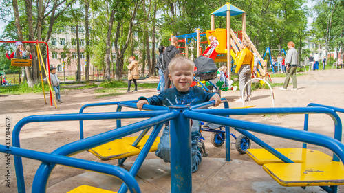 A three-year-old blond boy in a leisure park rides on a children's mechanical carousel. Mood Color - Blue