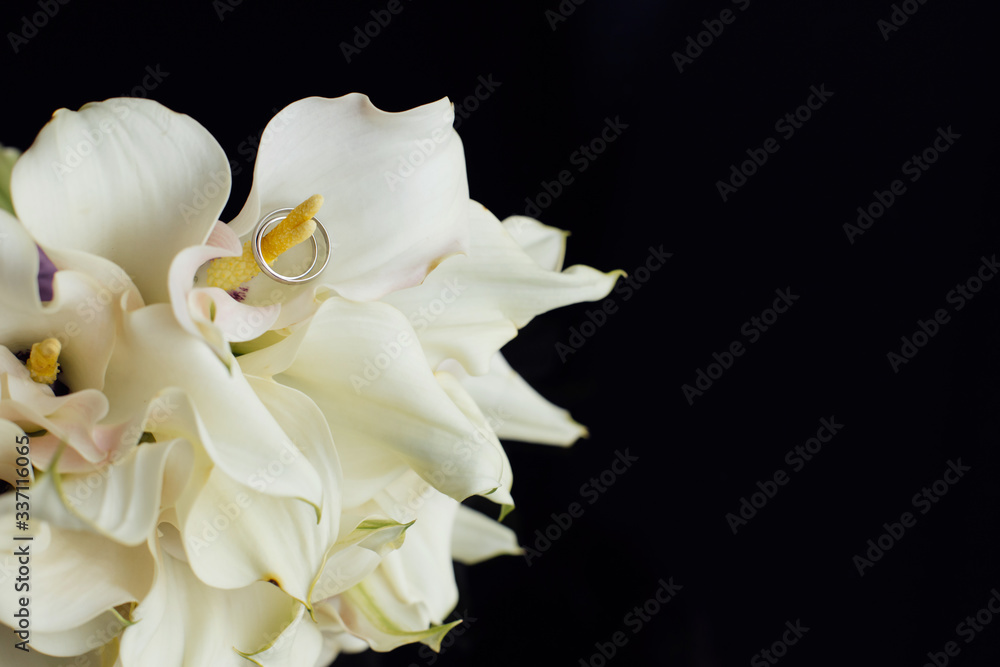 Wedding rings and a bouquet of callas on a black background.