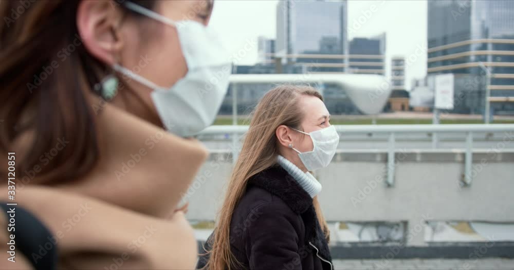 Epidemic protection. Two young happy Caucasian business women wear face masks walking on city street during quarantine. Epidemic protection. Two young happy Caucasian business women wear face masks walking on city street during quarantine.
