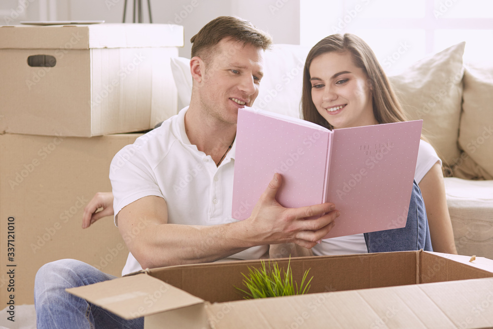 Portrait of happy couple looking at laptop computer together sitting in new house, surrounded with boxes Portrait of happy couple looking at laptop computer together sitting in new house, surrounded with boxes