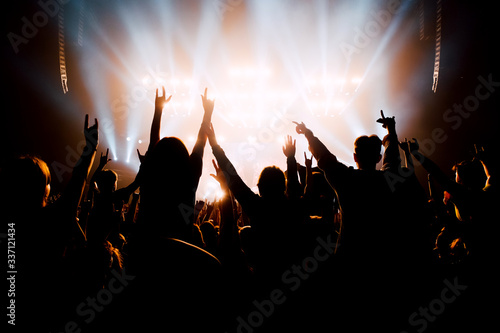 Crowd of people with raised up hands to the stage. Silhouettes in bright stage lights.