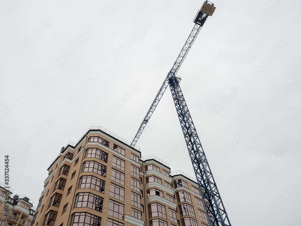 Fototapeta premium A blue tower crane stands next to a beige new home.