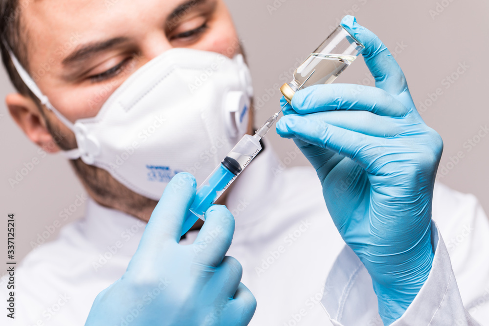 COVID-19 infection. Male doctor examines medicine for illness, man in blue mask with syringe and jar COVID-19 infection. Male doctor examines medicine for illness, man in blue mask with syringe and jar
