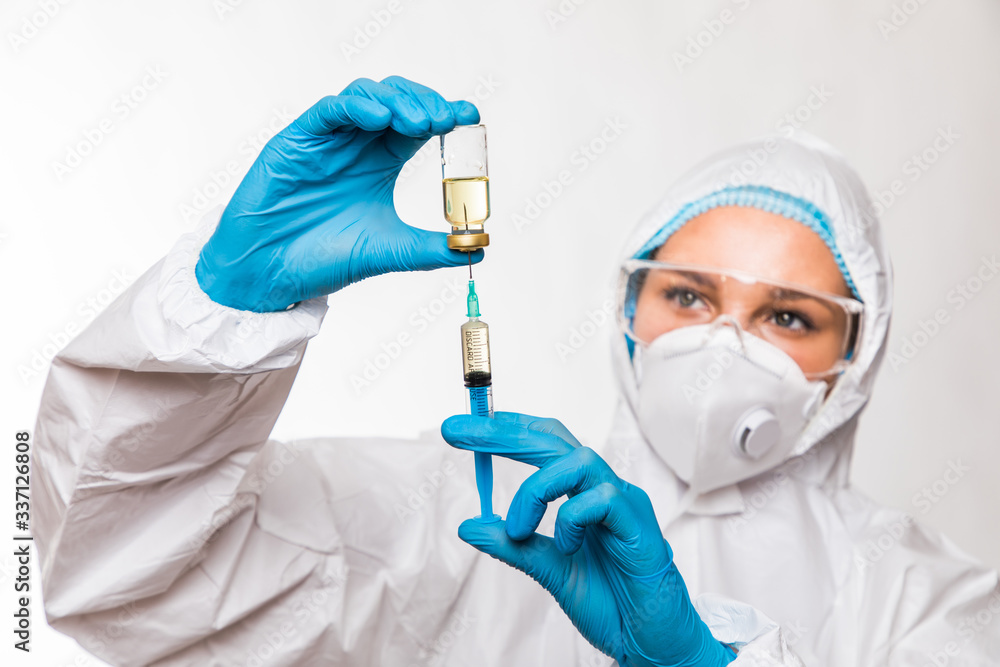 Female doctor in a protective white suit with a syringe in his hands and blue rubber gloves stands in different poses on a white background. Female doctor in a protective white suit with a syringe in his hands and blue rubber gloves stands in different poses on a white background.