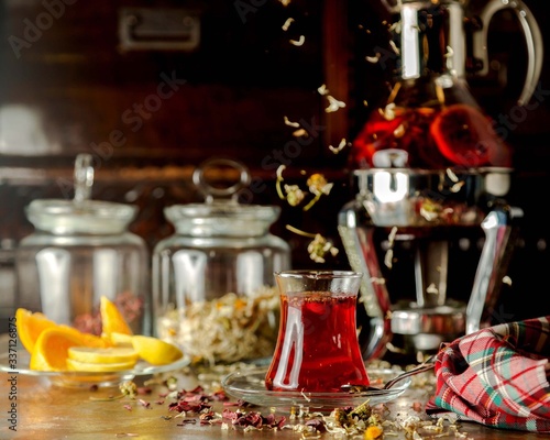 a glass of herbs tea next to lemon slices and glass tea pot